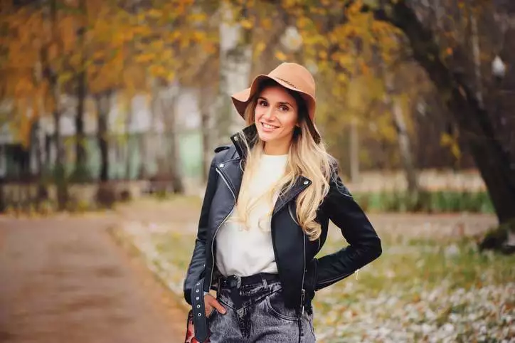 fashion autumn portrait of young happy woman walking outdoor in fall park in hat and leather jacket