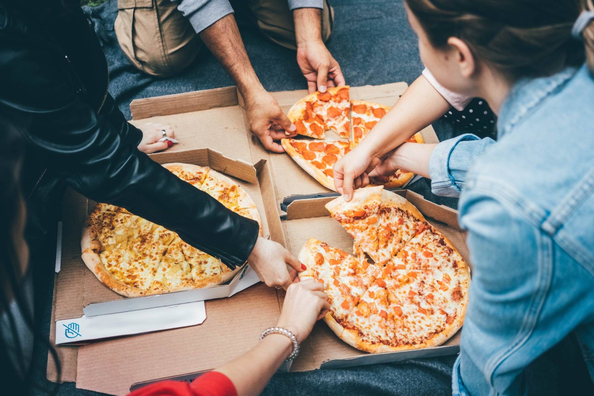 Top view people grab slices of pizza from box at the outdoors picnic. Unleash Your Taste Buds at the Best Places to Eat in The Colony